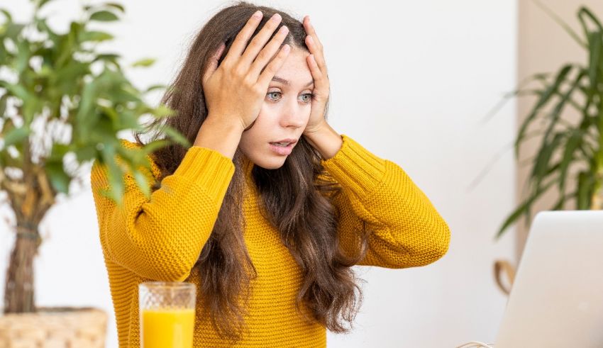 A woman is holding her head in front of her laptop.