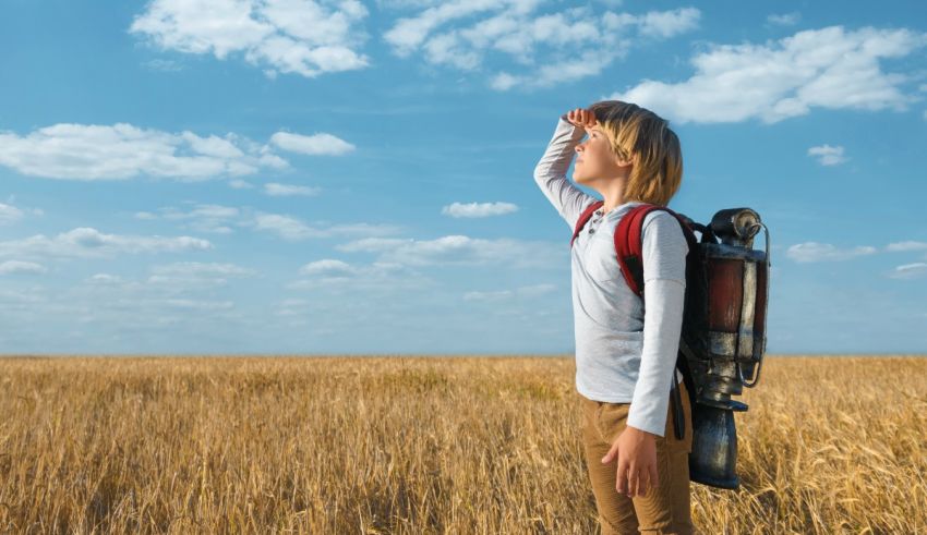 A girl with a backpack is standing in a wheat field.