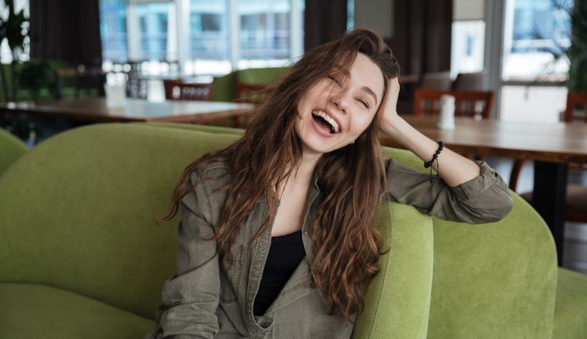 A young woman laughing while sitting on a green couch.