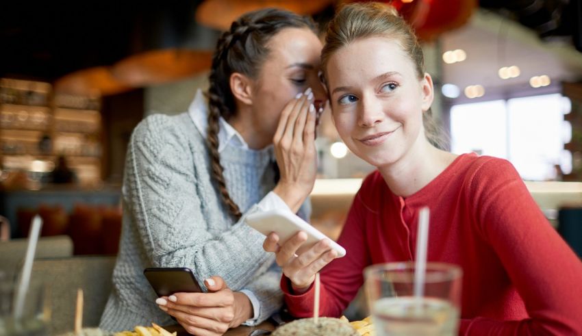 Two girls sitting at a table with a cell phone in their hands.