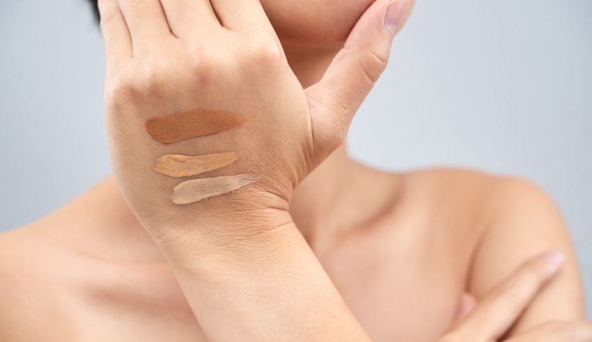 A woman is holding three different shades of concealer on her hand.