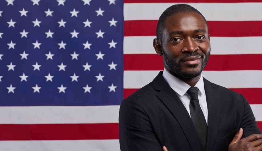 A black man with his arms crossed in front of an american flag.