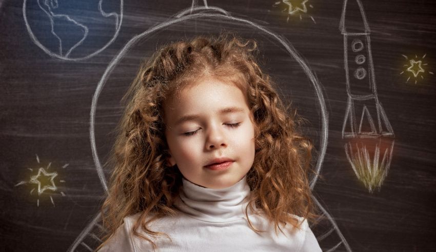 A little girl is standing in front of a chalkboard with rockets drawn on it.