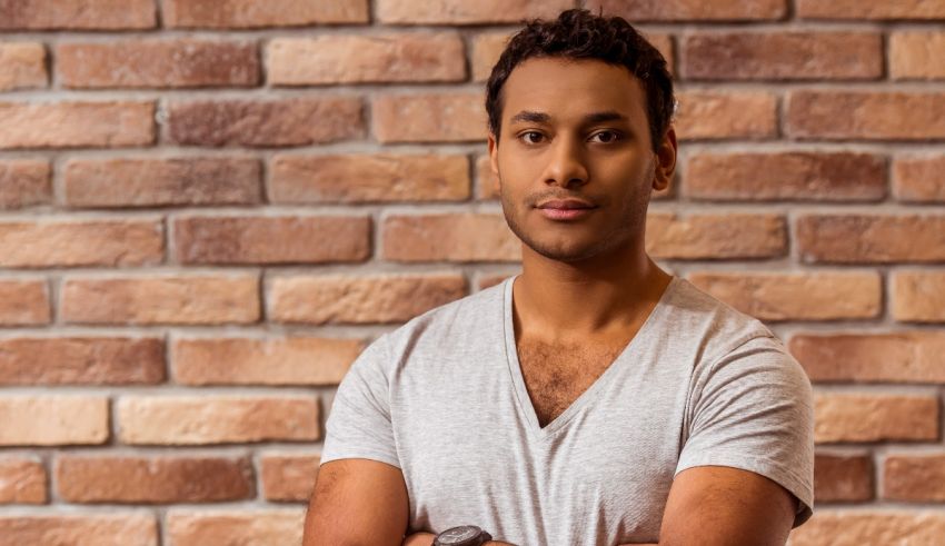 A young man with his arms crossed in front of a brick wall.