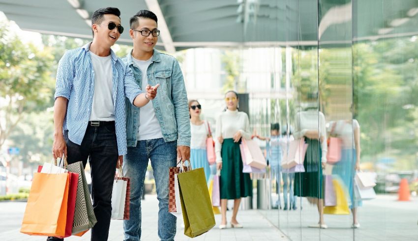 Two asian men holding shopping bags in front of a glass wall.