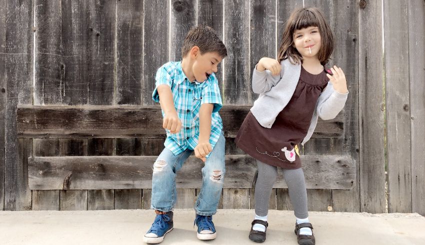 Two children standing in front of a wooden fence.