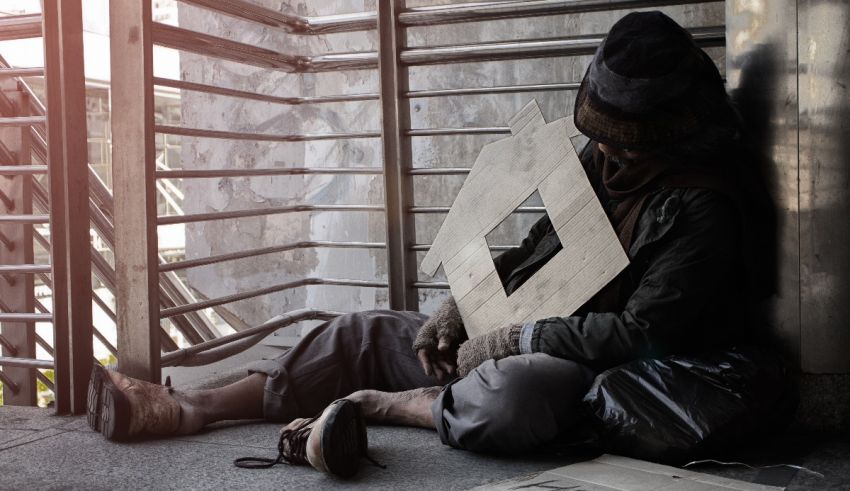 A homeless man sitting on the ground holding a piece of paper.