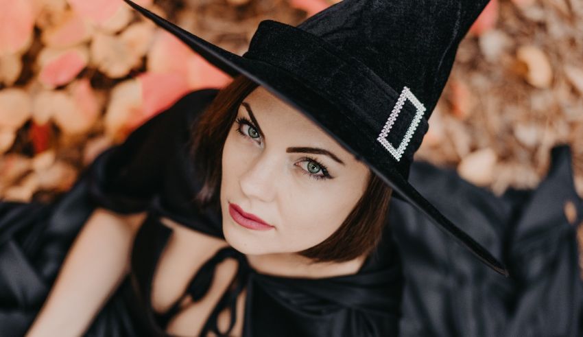 A woman in a black witch hat laying on leaves.
