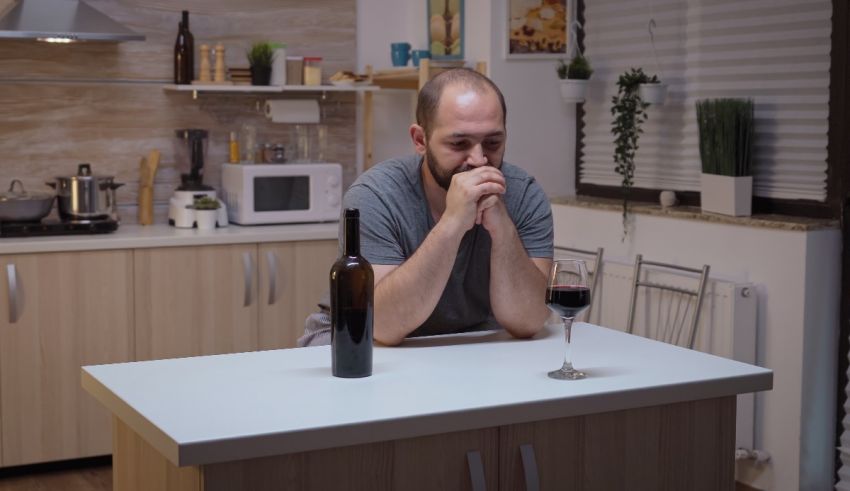 A man sitting at a kitchen table with a glass of wine.