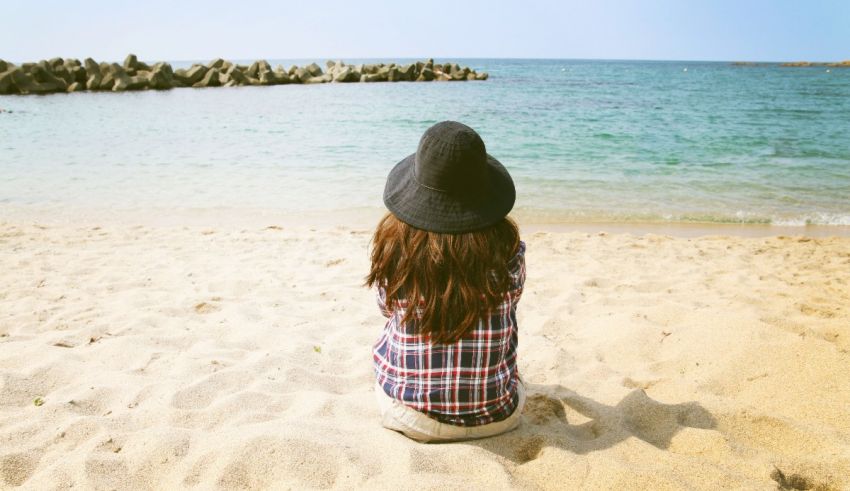A woman sitting on the beach with a hat on.