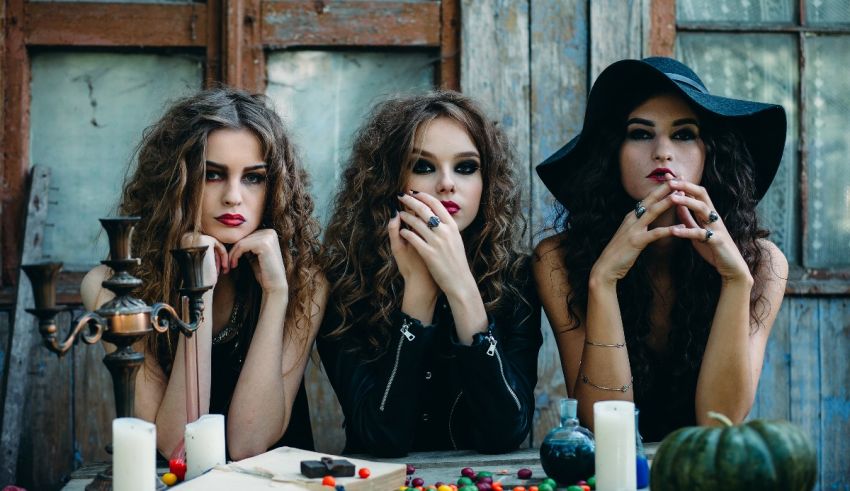 Three witches sitting at a table with candles.