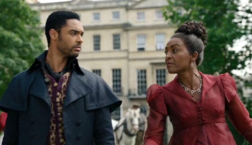 A man and woman in a red coat standing next to a horse.