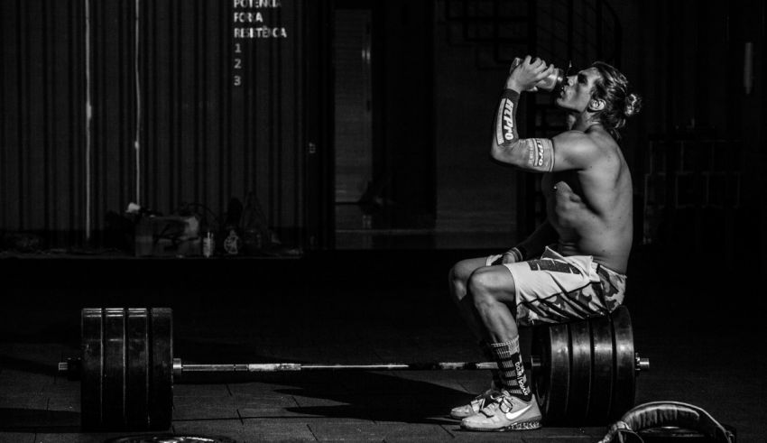 A man sitting on a barbell in a gym.