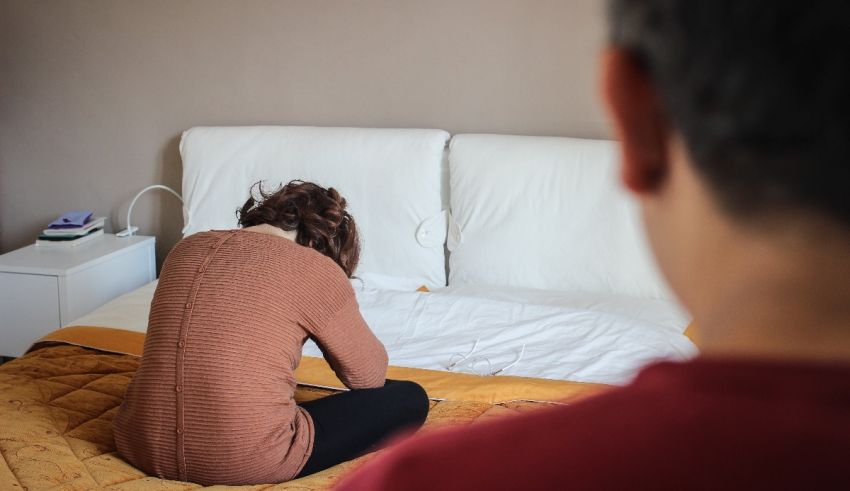 A man and woman sitting on a bed looking at each other.