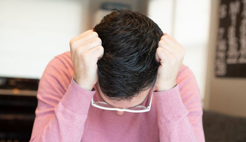 A man is holding his head in his hands while sitting at a desk.