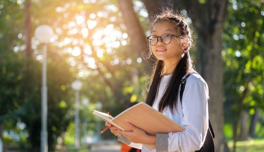 A young asian girl wearing glasses and holding a book.