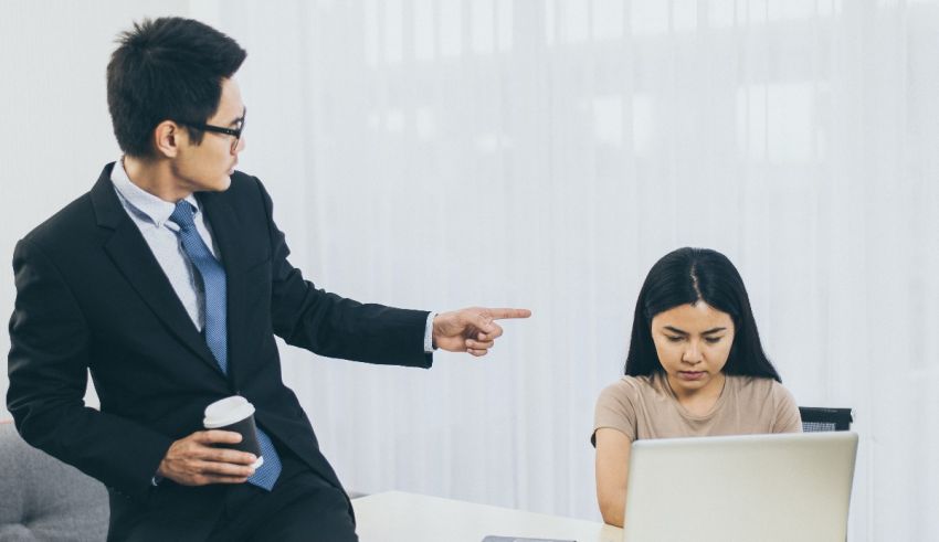 A man in a suit is pointing at a woman in an office.