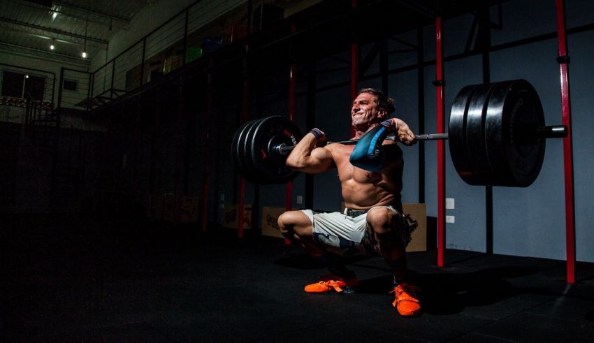 A man squatting with a barbell in a gym.
