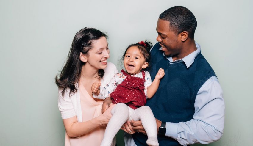 A man and woman holding a baby in front of a green background.