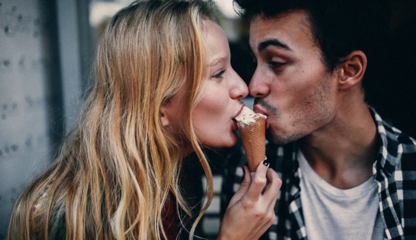 A man and woman kissing while eating an ice cream cone.