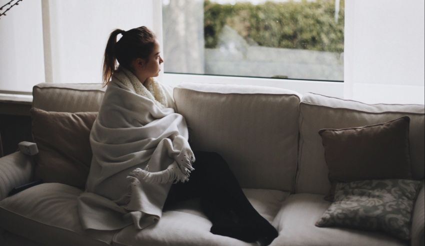 A woman sitting on a couch with a blanket wrapped around her.