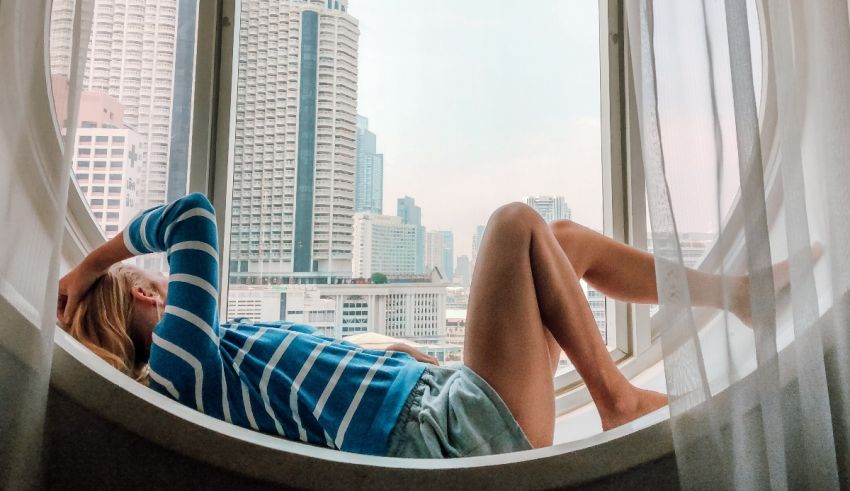 A woman relaxes in a round window with a view of a city.