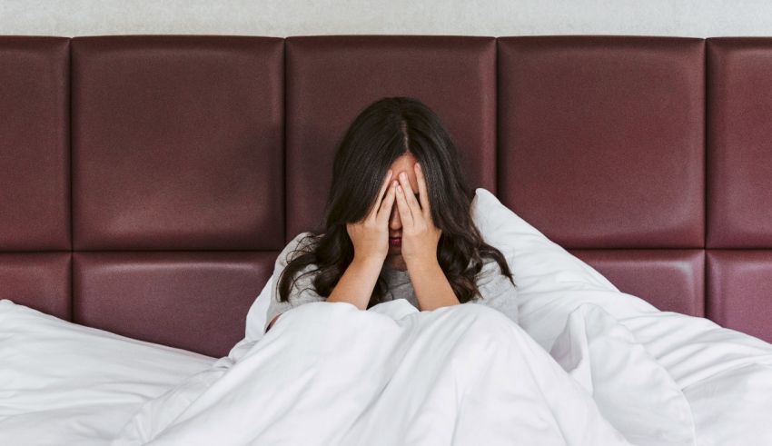 A woman is lying in bed with her hands covering her face.