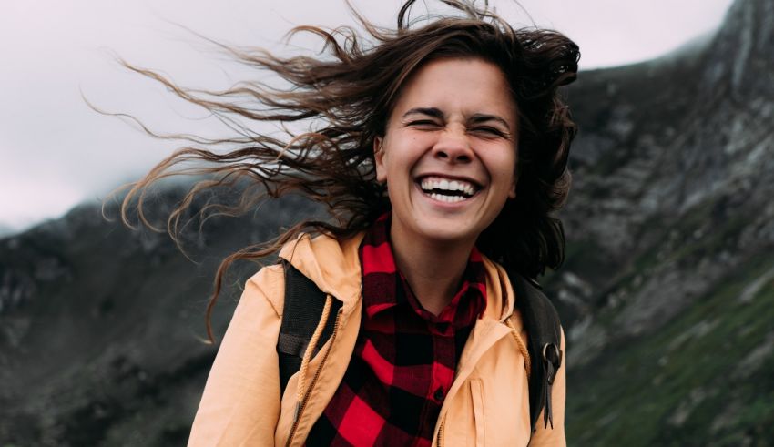 A woman laughing in the mountains with her hair blowing in the wind.