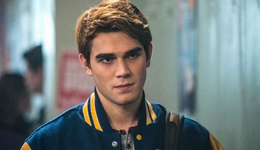 A young man in a blue and yellow jacket is standing in a hallway.