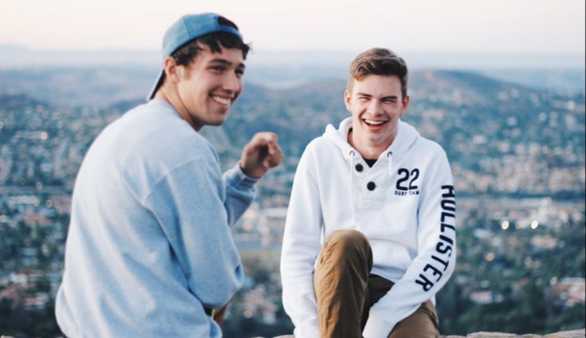 Two young men sitting on top of a mountain.