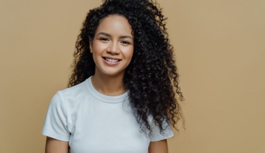 A young woman with curly hair smiling against a beige background.