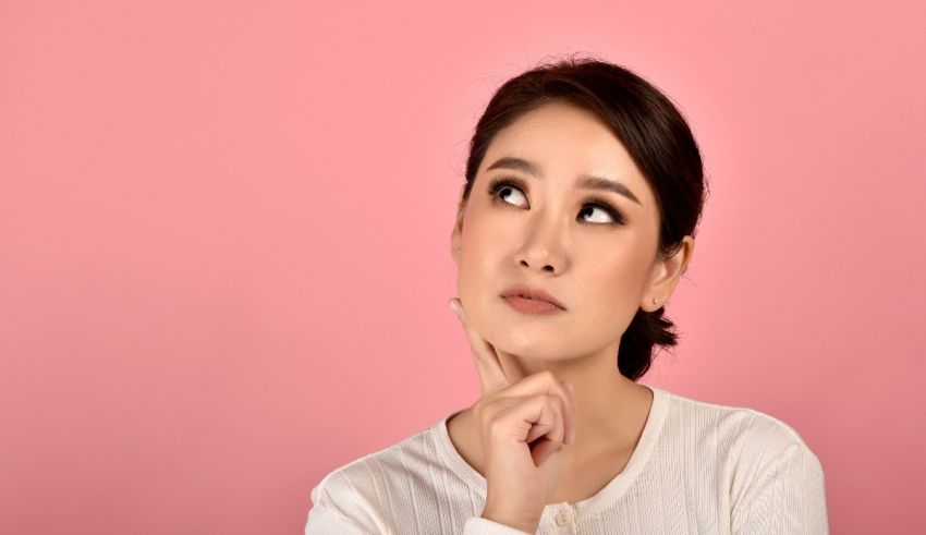 Young asian woman thinking on pink background.