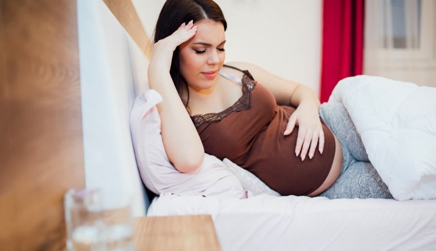 A pregnant woman laying in bed with her hand on her head.