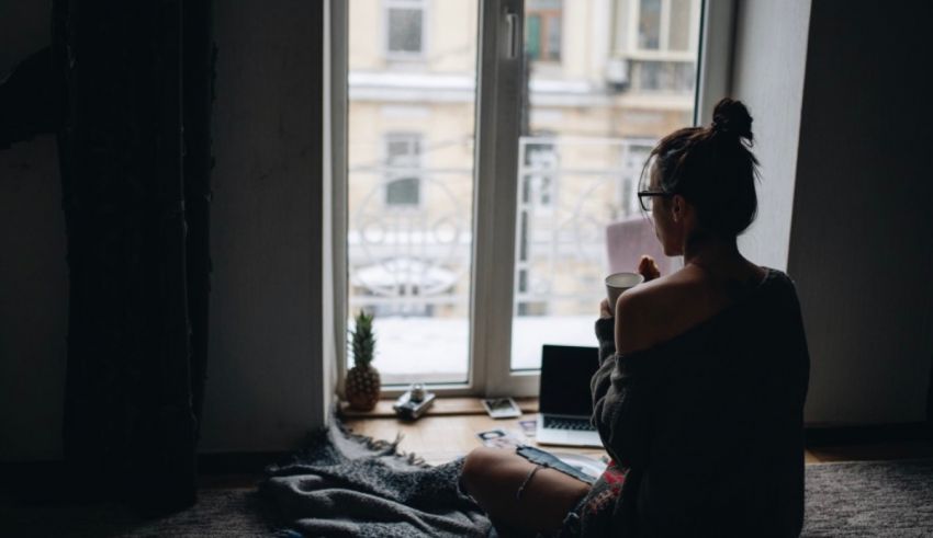 A woman sitting on the floor with a laptop in front of a window.