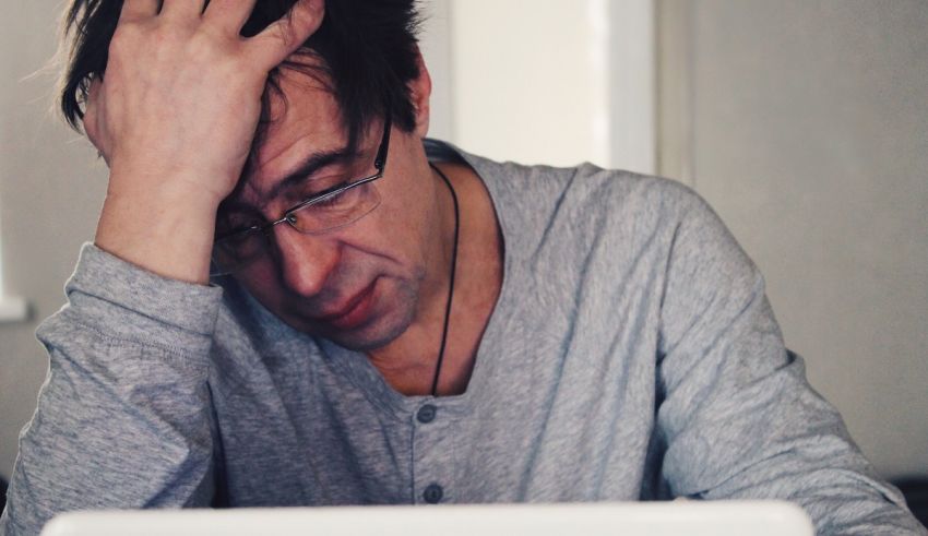 A man sitting at his computer with his hand on his head.