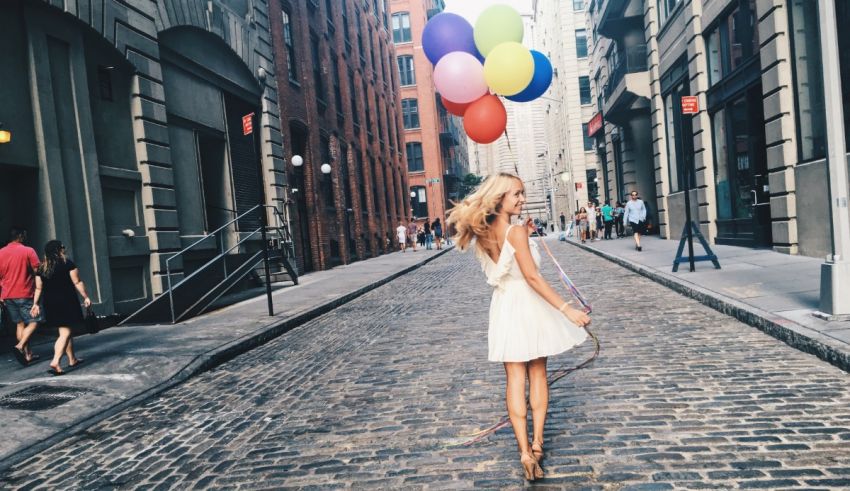 A woman in a white dress walking down a cobblestone street with colorful balloons.