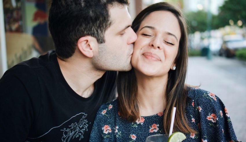 A man and woman kissing each other while holding a drink.