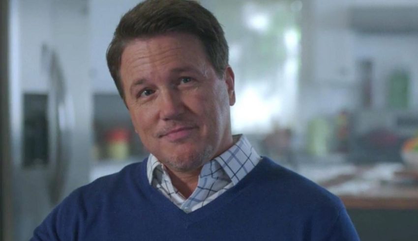 A man in a blue sweater standing in a kitchen.