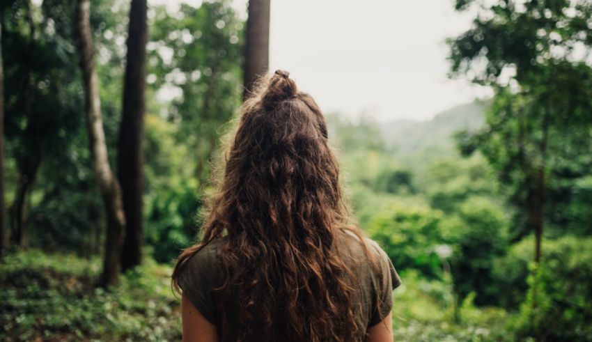 A woman with long curly hair standing in a forest.