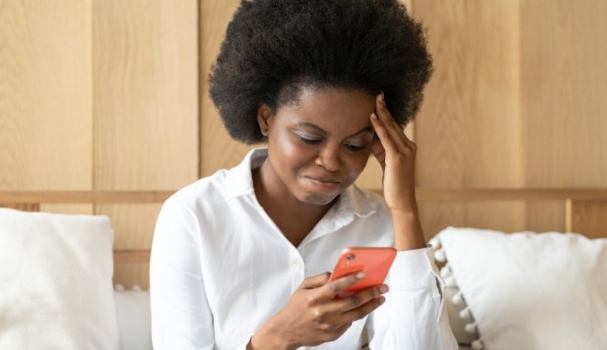 A black woman looking at her phone while sitting on a bed.