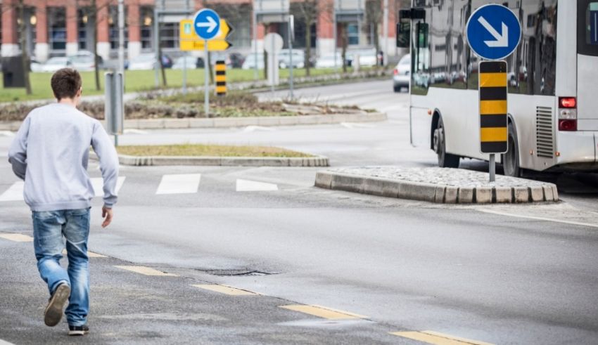A young man crossing the street in front of a bus.