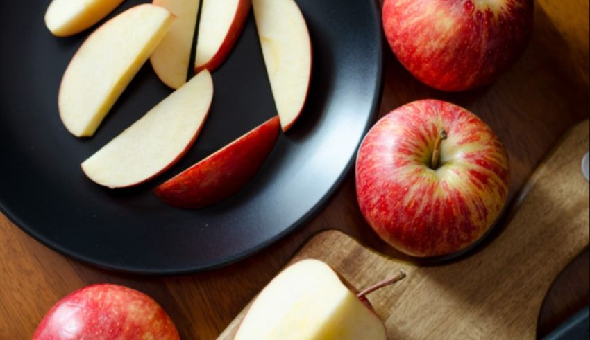 Sliced apples on a black plate next to a knife.