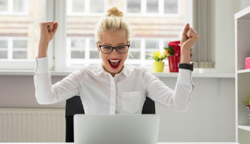 A woman is sitting in front of a laptop with her arms raised.
