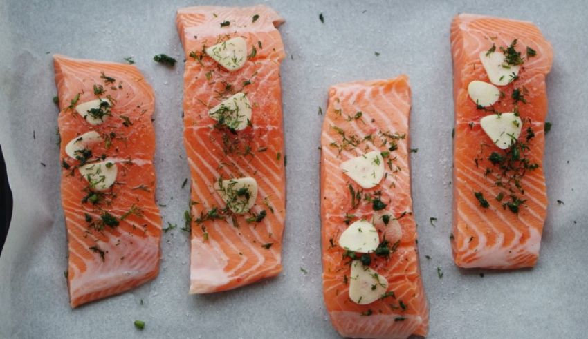 Four salmon fillets with herbs on a baking sheet.