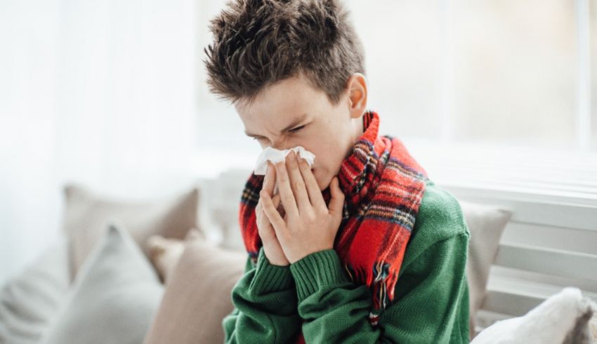 A boy blowing his nose while sitting on a couch.