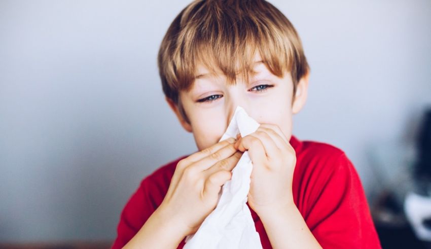 A young boy blowing his nose with a tissue.