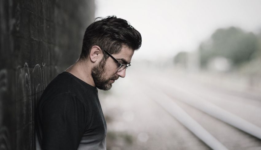 A man leaning against a wall next to a train track.