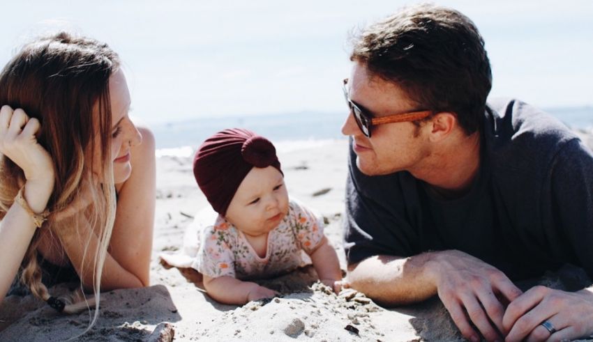 A man and woman laying on the beach with a baby.