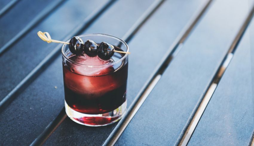 A drink with ice and black olives on a table.