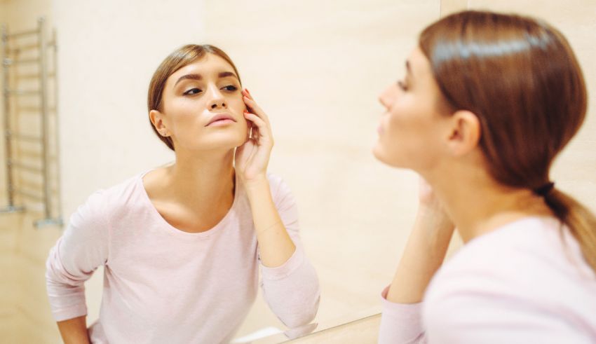 A woman is looking at her face in the mirror.